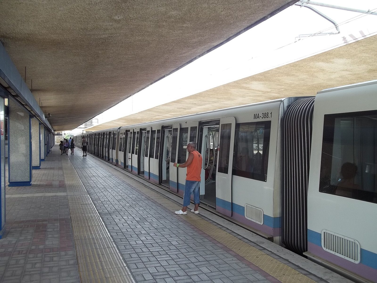 Un treno bianco con fasce azzurre e viola della linea Roma-Lido fermo con le porte aperte alla banchina coperta della stazione Cristoforo Colombo, con alcuni passeggeri sul marciapiede